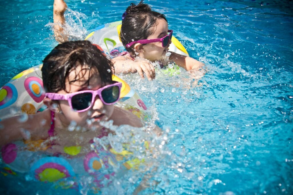 pexels-photo-61129-61129 Two young girls enjoying a playful day in a bright blue swimming pool with colorful float rings.